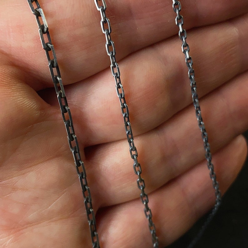 May include: Three silver chains of different thicknesses, laid out on a hand.