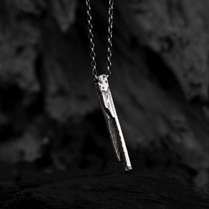 Puede incluir: Un collar de plata con un colgante rectangular largo y texturizado.