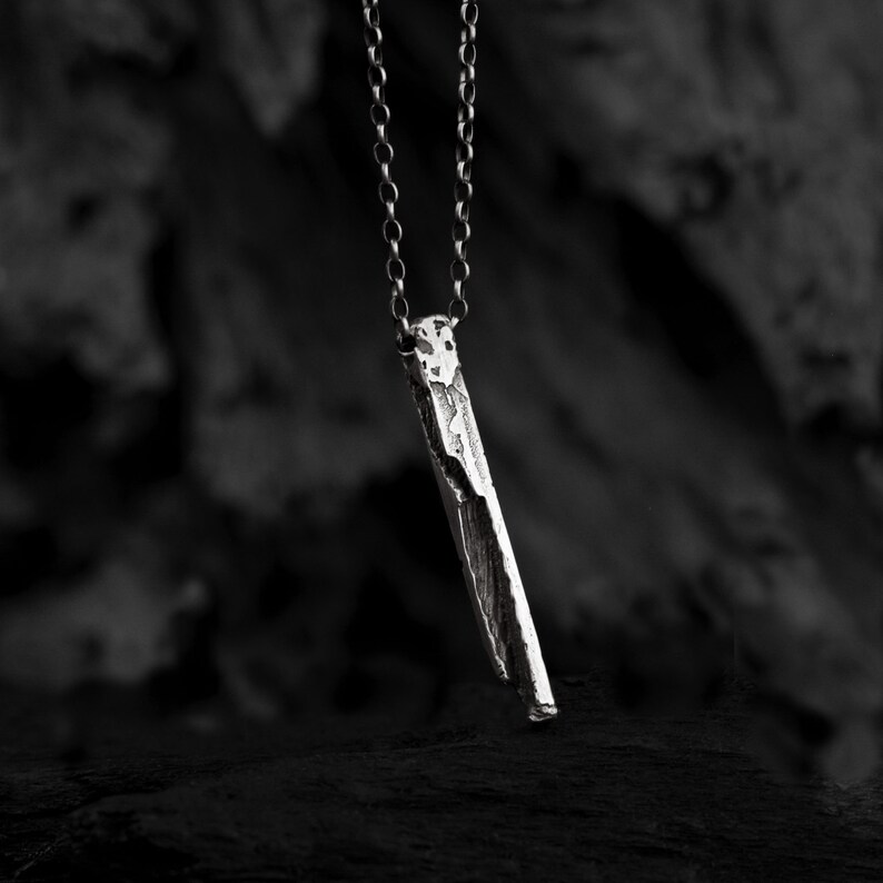 Puede incluir: Un collar de plata con un colgante rectangular largo y texturizado.