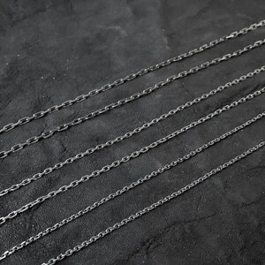May include: A set of eight silver chain necklaces of varying lengths and thicknesses, displayed on a dark gray background.