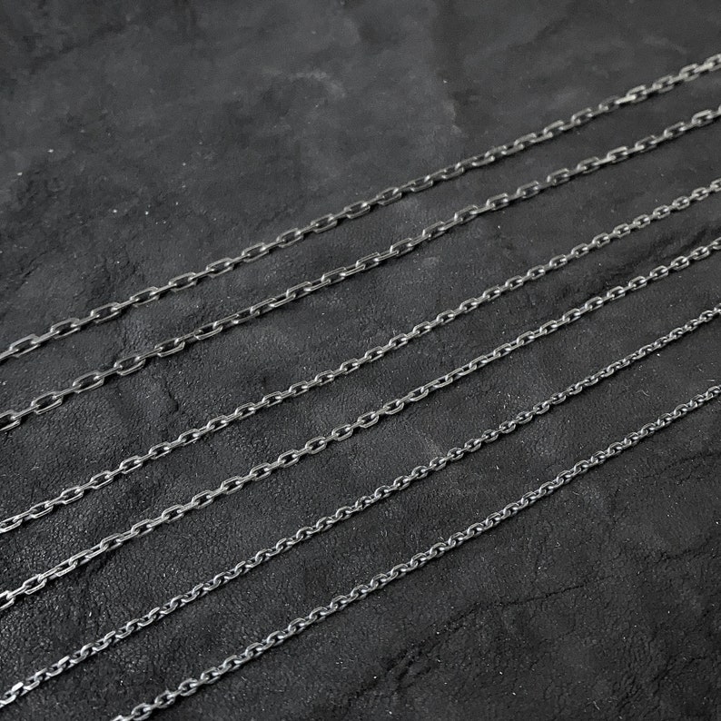 May include: A set of eight silver chain necklaces of varying lengths and thicknesses, displayed on a dark gray background.