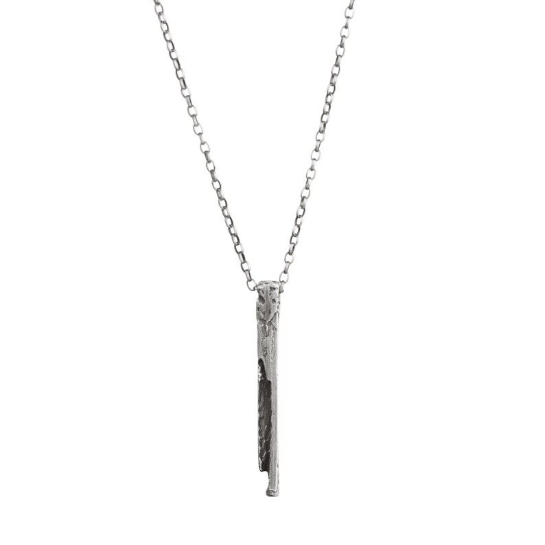 Puede incluir: Un collar de plata con un colgante largo, delgado y texturizado. El colgante es de forma rectangular simple con un borde ligeramente irregular.