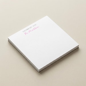 Könnte beinhalten: Ein Stapel weißes Notizpapier mit dem Text "NACHRICHT VON Fr. Müller" in rosa Schrift. Das Papier ist rechteckig und unbenutzt. Der Hintergrund ist einfarbig und neutral.