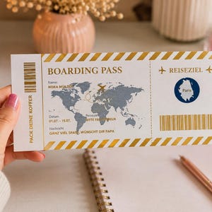 Könnte beinhalten: Eine weiße Bordkarte mit goldenen diagonalen Streifen an den oberen und unteren Rändern. Die Karte zeigt eine graue Weltkarte, den Text BOARDING PASS, Name: NORA MÜLLER, Datum 01.07.-15.07., REISEZIEL Paris und den deutschen Text PACK DEINE KOFFER.