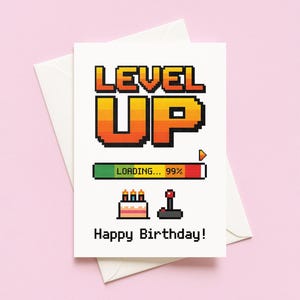 Könnte beinhalten: Eine weiße Geburtstagskarte mit einem Pixel-Design. Auf der Karte steht "LEVEL UP" in orange und gelb. Sie zeigt auch eine Ladeanzeige, einen Kuchen, einen Joystick und den Text "Happy Birthday!" auf rosa Hintergrund.