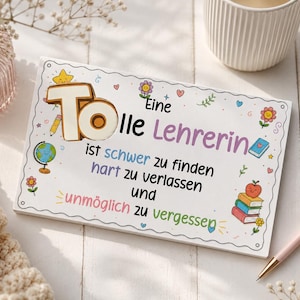 Pode incluir: Uma placa retangular branca com o texto em alemão "Eine Tolle Lehrerin ist schwer zu finden hart zu verlassen und unmöglich zu vergessen" e ilustrações coloridas de um globo, livros, uma maçã, flores e uma estrela.