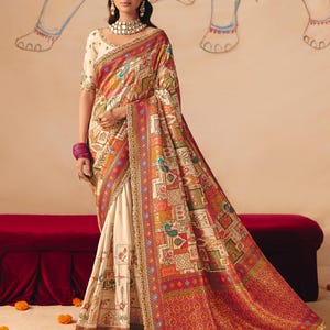 Peut inclure: Un sari crème avec un motif vibrant et coloré dans les tons de rouge, orange, vert et bleu. Le sari présente des détails complexes et une bordure décorative. Le modèle porte un chemisier et des bijoux assortis.