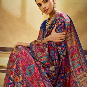 May include: A navy blue saree featuring a vibrant, multi-coloured floral and paisley pattern in shades of red, pink, orange, and teal. The fabric is adorned with intricate, dense embroidery throughout, including a wide, decorative border.