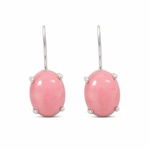 May include: A pair of earrings featuring oval, light pink gemstones set in silver-colored metal. The gemstones are held in place by four prongs. The earrings have a simple, elegant design.
