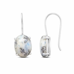 Peut inclure: Une paire de boucles d'oreilles pendantes en argent avec des pierres d'agate dendritique ovales. Les pierres sont blanches avec des nuances bleutées et des inclusions noires en forme de fougère. Chaque boucle est fixée par un crochet en argent.