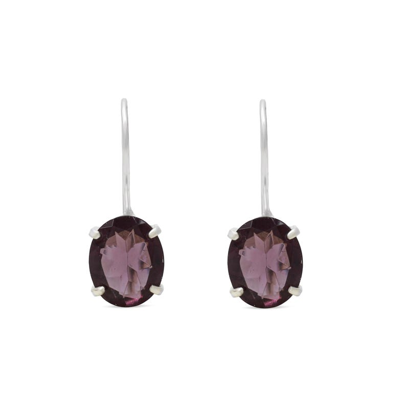May include: A pair of drop earrings featuring oval-shaped, deep purple faceted gemstones set in silver-toned metal prongs. Each earring is suspended from a simple, curved silver-toned hook wire, showcasing a clear, polished finish on the stones.
