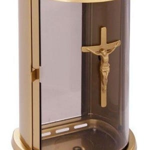Könnte beinhalten: Ein goldfarbener Votivkerzenhalter mit einer durchsichtigen Glasfront und einem goldenen Kreuz mit einer Jesusfigur. Der Kerzenhalter hat eine abgerundete Ober- und Unterseite und eine Tür an der Seite.