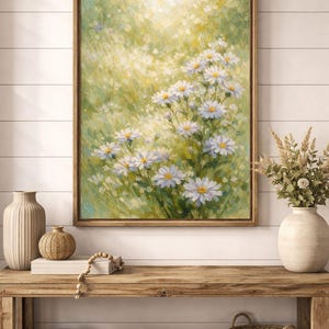 Op de afbeelding: Een ingelijst bloemenschilderij met witte madeliefjes met gele centra tegen een groen-gele achtergrond. Het hangt boven een houten console met vazen en gevlochten manden, wat een rustieke sfeer creëert.