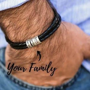 May include: Black braided leather bracelet with silver beads engraved with names. The bracelet is worn on a wrist, with the words "Your Family" in cursive script below.