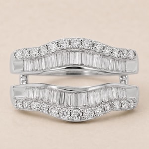 May include: A silver-toned ring guard featuring two curved bands connected at the sides. Each band is set with a row of baguette-cut stones in the center, bordered by a row of small, round, brilliant-cut stones along the outer edges.