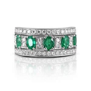 May include: A silver ring with oval emeralds and round diamonds. The emeralds are set in a row, alternating with the diamonds. The ring has a curved design and is set with small diamonds around the edges.