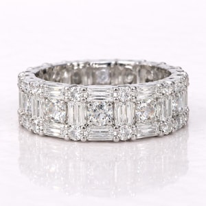 May include: A dazzling, white gold eternity ring. The ring features a continuous band of alternating round and baguette-cut diamonds, creating a sparkling, luxurious design. The diamonds are set closely together, maximizing brilliance.
