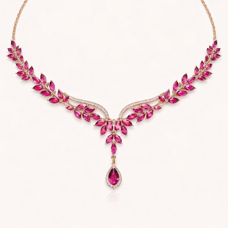 May include: A gold-toned necklace featuring a leaf-like design with vibrant pink gemstones. The necklace has a delicate chain and a central pendant with a teardrop-shaped stone, perfect for special occasions.