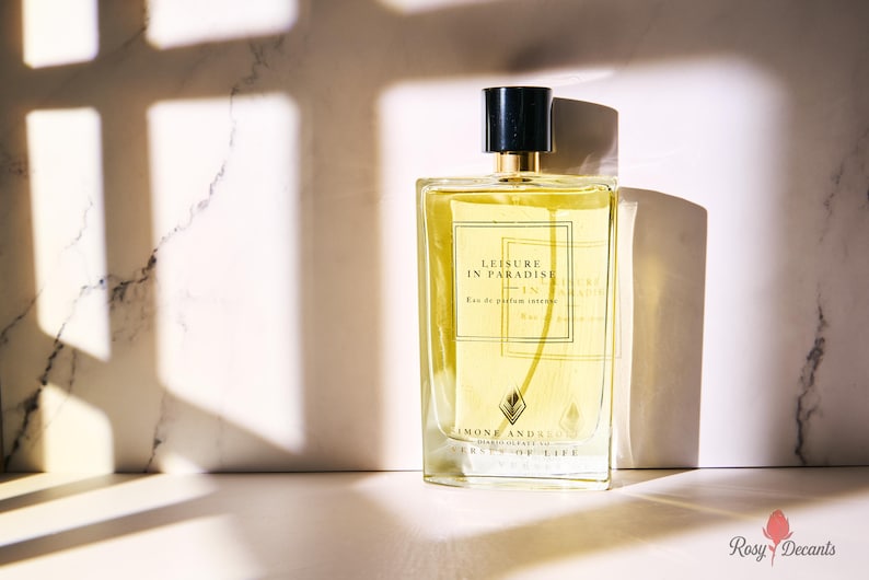K&ouml;nnte beinhalten: Ein rechteckiger Parf&uuml;mflakon mit schwarzem Verschluss und goldenen Akzenten. Die Flasche enth&auml;lt eine gelbe Fl&uuml;ssigkeit und tr&auml;gt den Text "LEISURE IN PARADISE" und "SIMONE ANDREOLI". Der Hintergrund ist eine Marmoroberfl&auml;che mit Schatten.