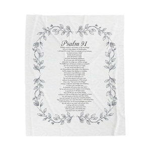 May include: A white blanket featuring the text of Psalm 91 in black script, framed by a grey floral wreath. This soft, neutral-toned blanket is a decorative home item.