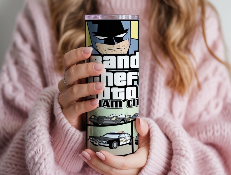May include: A cylindrical stainless steel tumbler featuring a graphic print of a comic book style Batman character at the top, the text Grand Theft Auto Gotham City in the center, and illustrations of a black sports car and a police car below.