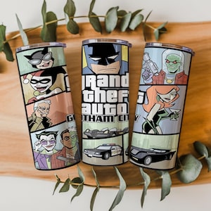 May include: Three cylindrical metal tumblers featuring a comic book style graphic print. The designs include illustrations of various characters, a police car, and a black vehicle, with the text Grand Theft Auto Gotham City displayed prominently.