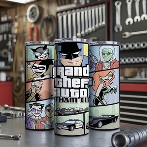 May include: Three cylindrical tumblers featuring a comic book style graphic wrap. The design displays various characters including Batman, Harley Quinn, and the Joker, alongside the text Grand Theft Auto Gotham City and illustrations of vehicles.
