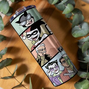 May include: A cylindrical stainless steel tumbler featuring a wrap-around graphic print of comic book characters including Catwoman, Harley Quinn, Commissioner Gordon, The Joker, and Two-Face, topped with a clear plastic lid and a sliding closure.