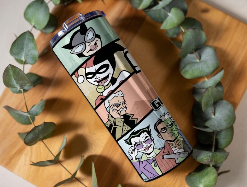 May include: A cylindrical stainless steel tumbler featuring a wrap-around graphic print of comic book characters including Catwoman, Harley Quinn, Commissioner Gordon, The Joker, and Two-Face, topped with a clear plastic lid and a sliding closure.
