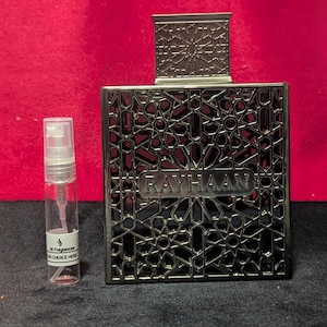Könnte beinhalten: Eine silberne Parfümflasche mit einem komplizierten geometrischen Design und dem Wort "RAYHAAN" in einem rechteckigen Rahmen. Daneben befindet sich ein kleines, klares Probenfläschchen mit dem Etikett "Hi Fragrances, Your Choice Here".
