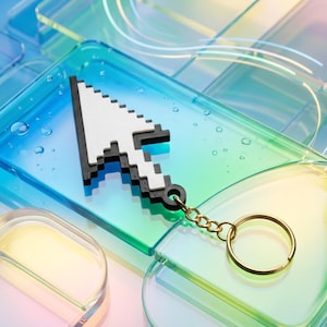 May include: A pixelated white and black cursor keychain with a gold-colored chain and ring. The cursor is resting on a clear, rectangular surface with a blue and green gradient. The background is a similar, abstract design.