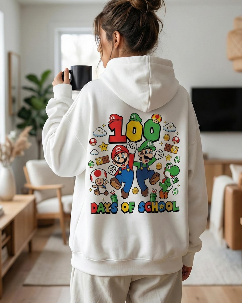 May include: White hoodie featuring a colorful graphic of Mario and Luigi with the text "100 Days of School." The design includes cartoon elements like stars, clouds, and mushrooms. The hoodie is a casual garment.