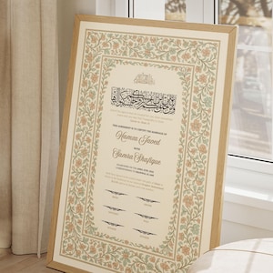 Könnte beinhalten: Gerahmte Heiratsurkunde mit ornamentalem Blumenrand in Beige, Pfirsich und Grün. Das Dokument enthält arabische Kalligraphie und die Namen "Hamza Javed" und "Samra Shafique". Der Rahmen ist aus hellem Holz.