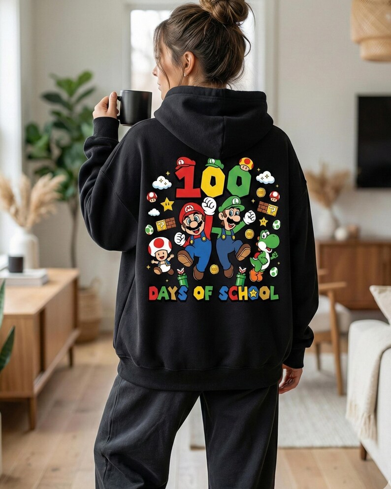 May include: Black hoodie featuring a colorful graphic of Mario and Luigi with the number 100 and the words "DAYS OF SCHOOL". The design includes mushrooms, stars, and other game elements. The hoodie is worn by a person.