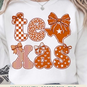 May include: White sweatshirt featuring the word "Texas" in orange and brown. The letters are patterned with a checkerboard, leopard print, stripes, and stars. Each letter is decorated with a bow. The Texas outline includes a star.