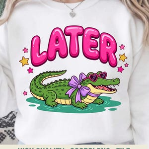 Puede incluir: Sudadera blanca con un cocodrilo de dibujos animados con gafas de sol en forma de corazón y un lazo morado. La palabra "LATER" está escrita en letras rosas con burbujas encima del cocodrilo, rodeada de estrellas. La parte inferior de la sudadera dice "HIGH QUALITY . 300DPI PNG . FILE".