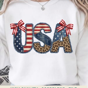 Op de afbeelding: Witte sweatshirt met het woord "USA" in een patchwork-ontwerp. De letters zijn voorzien van denim, luipaardprint en de Amerikaanse vlag. Rood-wit gestreepte strikken accentueren de bovenkant van de "U" en de "A".