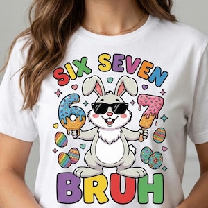 May include: White t-shirt with a colourful graphic featuring a cartoon bunny wearing sunglasses, holding ice cream shaped like the numbers 6 and 7. The word "BRUH" is below the bunny. The shirt also has the words "SIX SEVEN".