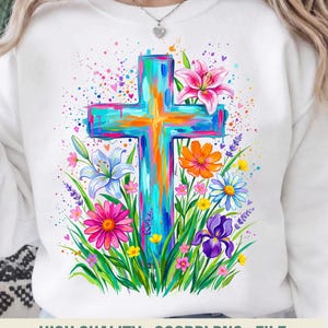 Könnte beinhalten: Weißes Sweatshirt mit einem farbenfrohen Kreuzdesign, umgeben von Blumen und Grün. Das Kreuz ist in leuchtenden Farben von Blau, Orange und Rosa gemalt. Das Design umfasst Lilien, Gänseblümchen und andere Blumen. Der Text unten lautet "HIGH QUALITY . 300DPI PNG . FILE".