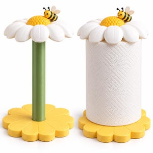 May include: Two paper towel holders featuring a yellow daisy-shaped base and a white daisy-shaped top with a small bee figurine. One holder has a green cylindrical stem, while the other holds a roll of white paper towels with a diamond pattern.