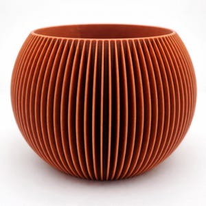 May include: A terracotta-colored, spherical planter with vertical, ridged detailing. The open top and rounded shape create a modern, minimalist design. The planter is suitable for indoor or outdoor use.