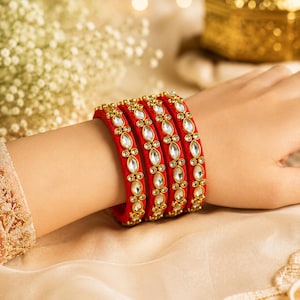 Peut inclure: Un ensemble de quatre bracelets rigides rouge vif ornés d'une rangée centrale de pierres claires taille marquise serties dans du métal doré. Chaque bracelet présente une texture lisse et un motif répétitif de petits accents dorés.