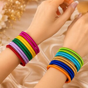 May include: A set of thin, smooth bangles in a vibrant rainbow of colors. The left wrist features magenta, yellow, green, lavender, and red bangles. The right wrist displays lime green, turquoise, gold, royal blue, and orange bangles.
