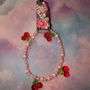 May include: A glitter-covered lighter with the word "PRINCESS" spelled out in letter beads. A pink and white beaded bracelet with heart-shaped beads and red cherry charms is attached to the lighter.