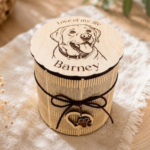 Könnte beinhalten: Eine zylindrische Dose aus hellem Holz mit einem lasergravierten Porträt eines Labradors auf dem Deckel. Der Text "Love of my life" und "Barney" ist über und unter dem Hund eingraviert. Eine dunkelbraune Schnur mit Herzanhänger ist umgebunden.