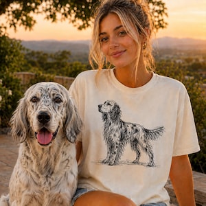 May include: A cream-coloured short-sleeve t-shirt featuring a black line-art illustration of an English Setter dog standing in profile. The graphic is centred on the chest of the garment, which has a crew neckline and a relaxed, casual fit.