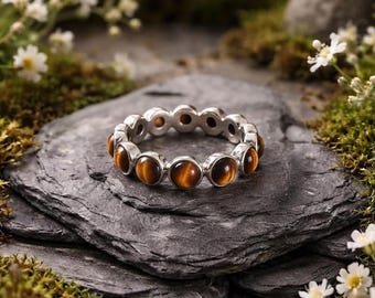 May include: A silver band ring featuring a continuous row of round, polished tiger's eye gemstones. Each stone displays a characteristic chatoyant golden-brown luster, securely set within individual silver bezels that form the circular ring structure.