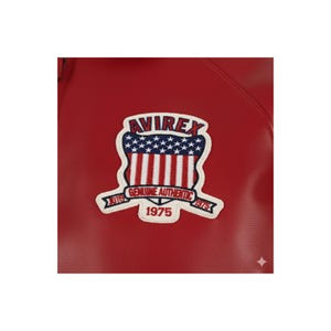 May include: Close-up of a red leather jacket featuring a white and blue patch. The patch has the word "AVIREX" at the top, a design of red and white stripes, and the text "GENUINE AUTHENTIC 1975".