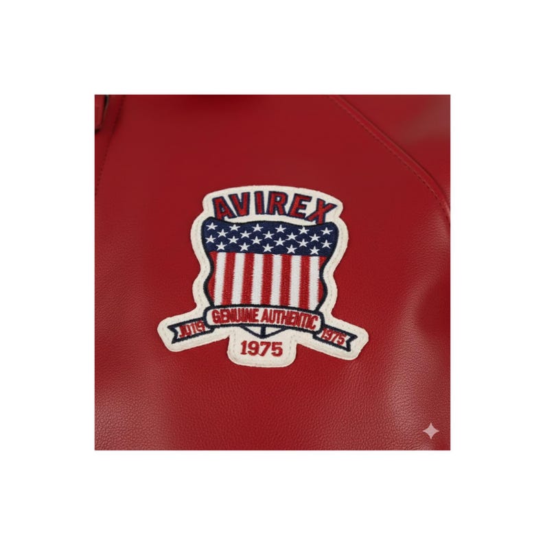 May include: Close-up of a red leather jacket featuring a white and blue patch. The patch has the word "AVIREX" at the top, a design of red and white stripes, and the text "GENUINE AUTHENTIC 1975".