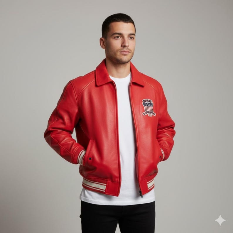 May include: A vibrant red leather jacket with a collared neckline and a zipper closure. The jacket features a patch on the chest with a hockey-themed design and striped detailing on the cuffs and hem. The model is wearing a white t-shirt and black pants.